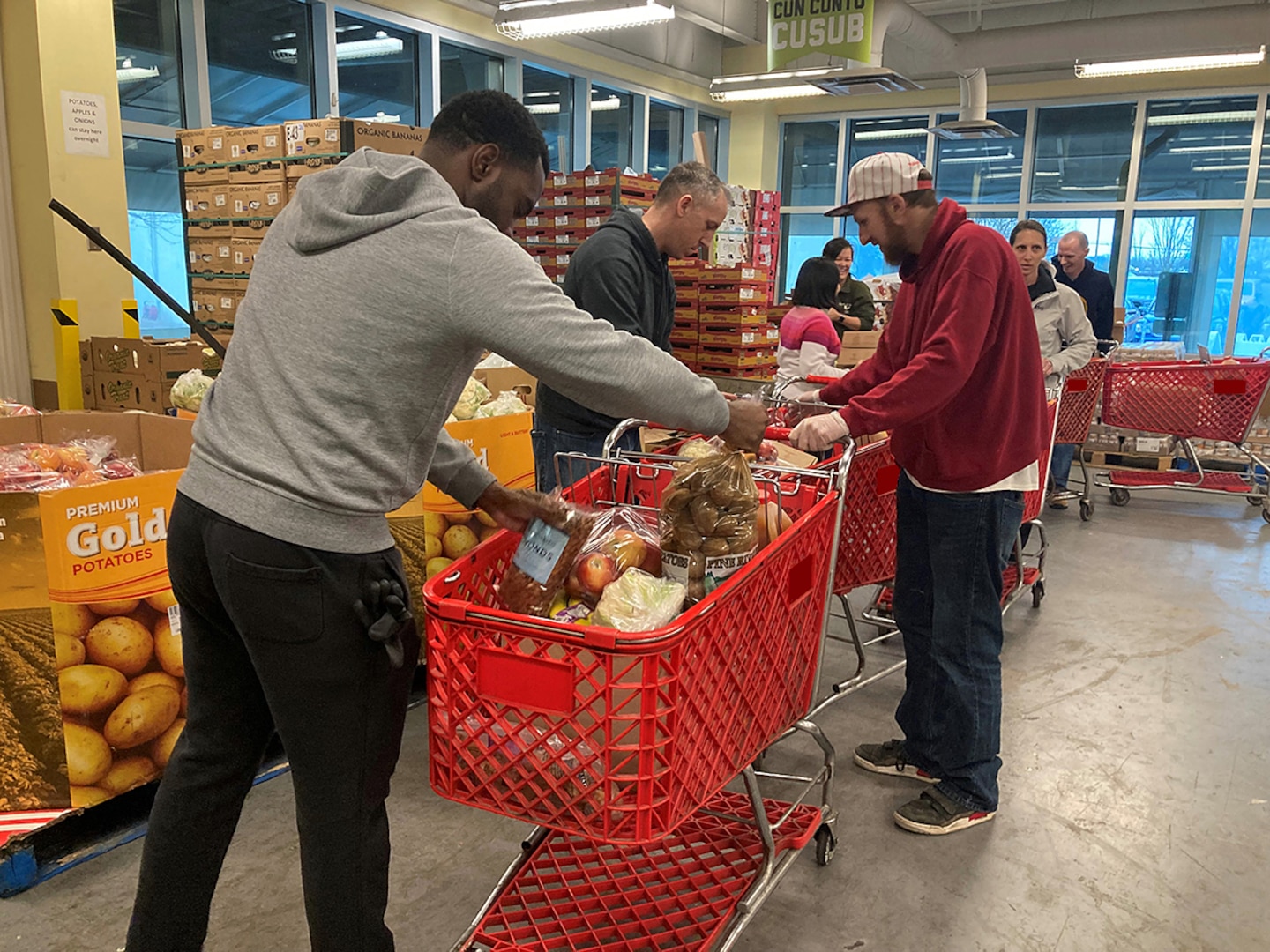 Several people wearing casual clothing load shopping carts full of food in a warehouse.