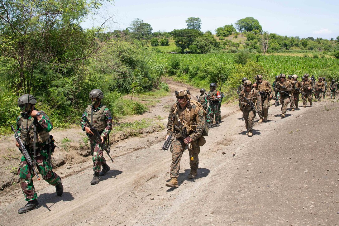 Soldiers march together down a dirt road.