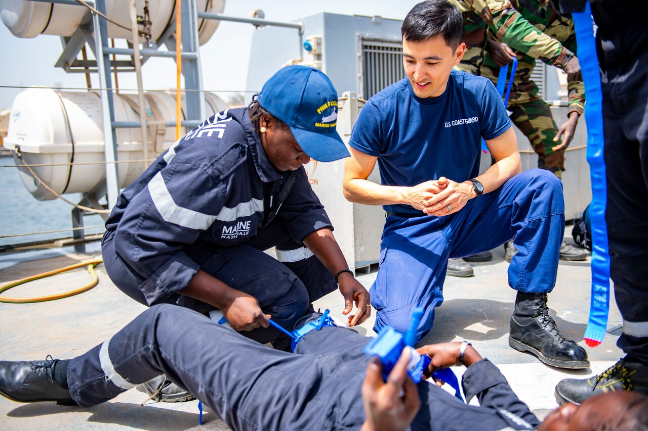 Two military personnel engage in medical training on the deck of a naval vessel.