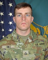 Man in U.S. Army uniform standing in front of two flags.