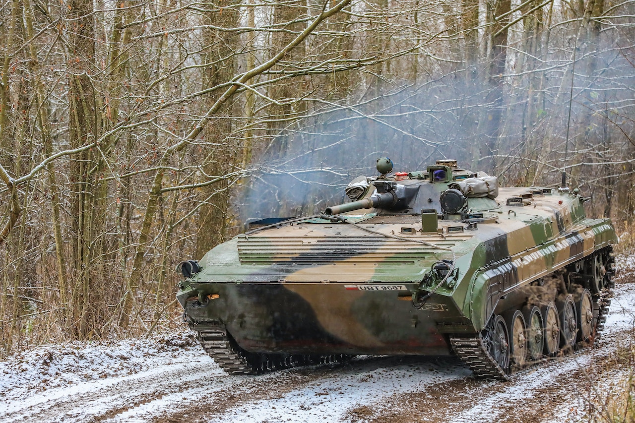 A tank rolls down a dirt road.