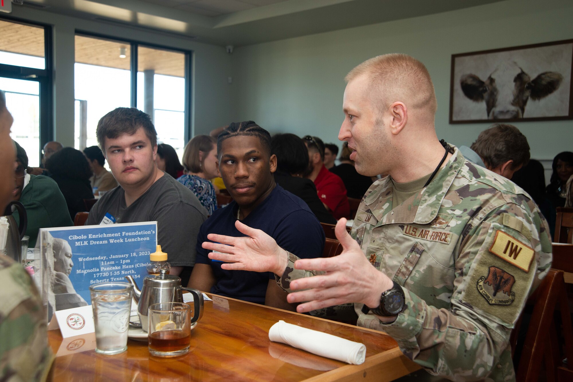 An officer in a camouflaged uniform talks with a student while both are sitting at a table.