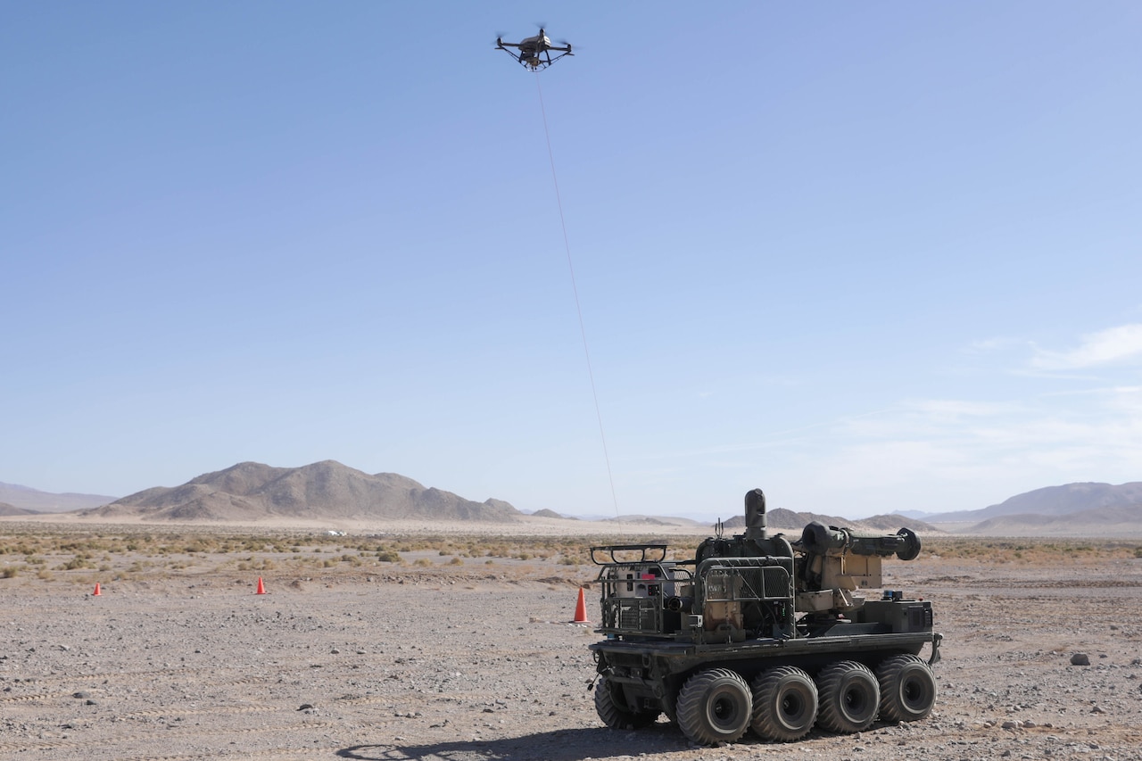 An unmanned aircraft is tethered to a military vehicle in a desert environment.