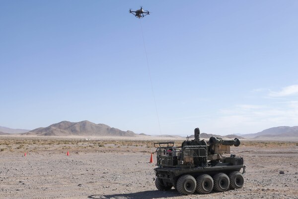 An unmanned aircraft is tethered to a military vehicle in a desert environment.