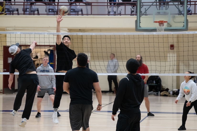 Airmen playing volleyball on a volleyball court.