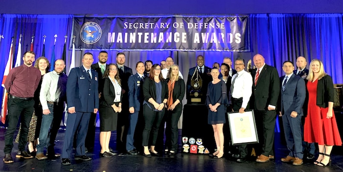 People posing for group photo with award in front of blue curtains