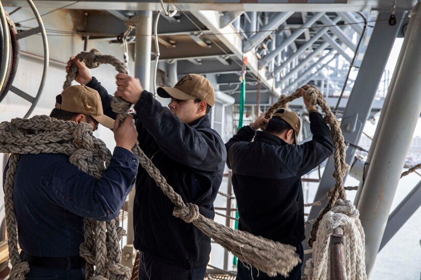 Sailors carry ropes around their shoulders.