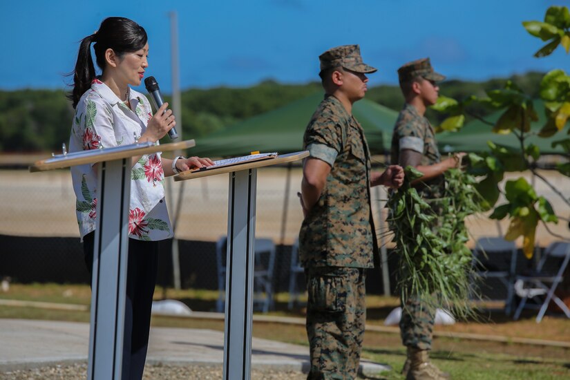 One person speaks with a microphone while two service members stand nearby.