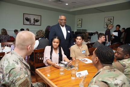 Two students and several military member talk at a table.
