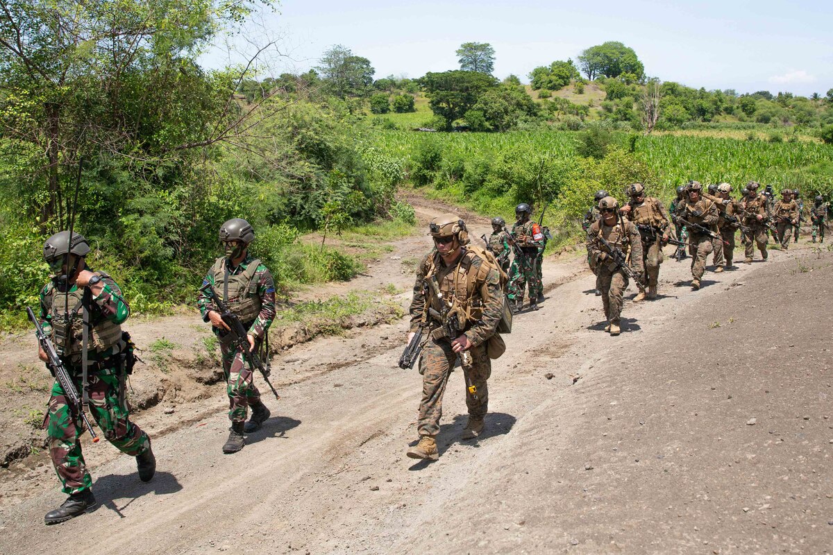 Soldiers march together down a dirt road.