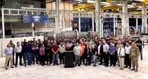 People posing for group photo with award in foreground and jet engine in background.