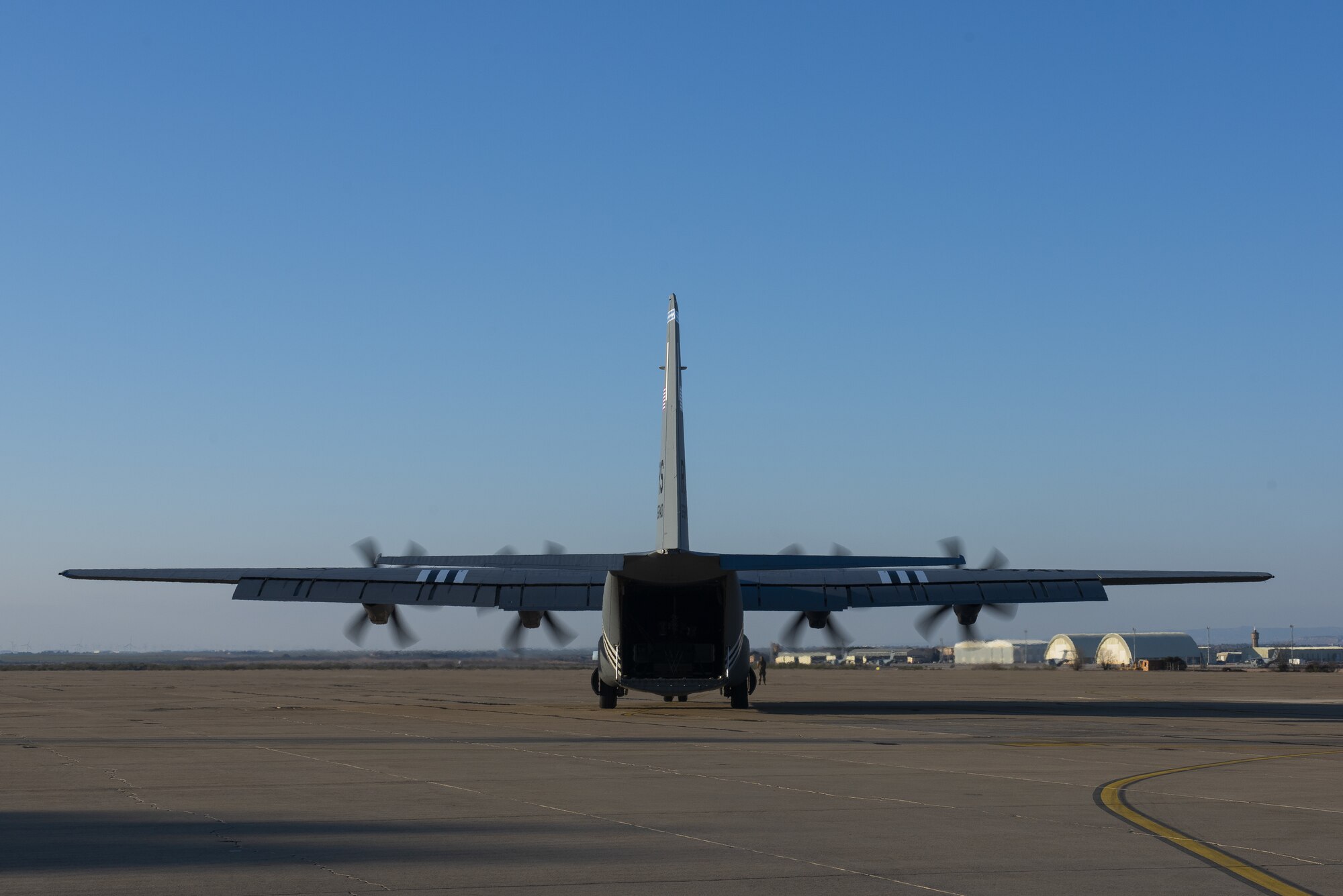 A grey aircraft sits on a runway with a bright blue sky