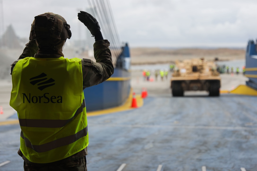 A soldier directs a vehicle onto a cargo ship