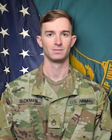 Man in U.S. Army uniform standing in front of two flags.