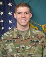 Man in U.S. Army uniform standing in front of two flags.