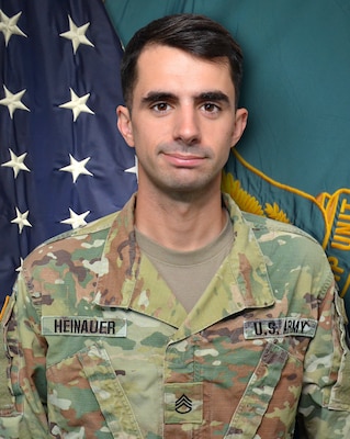 Man in U.S. Army uniform standing in front of two flags.