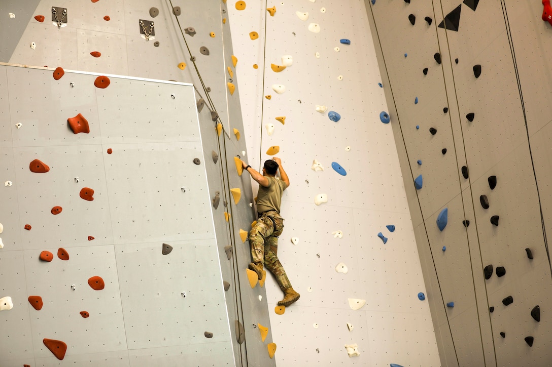 An Army mountaineering student climbs an indoor rock climbing wall.