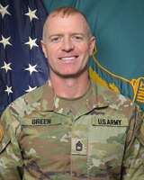 Man in U.S. Army uniform standing in front of two flags.
