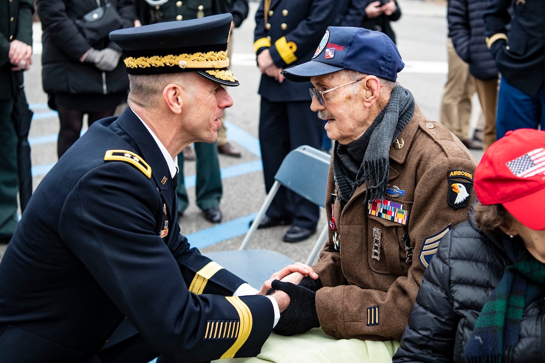 A soldier kneels to shakes hands with a veteran.