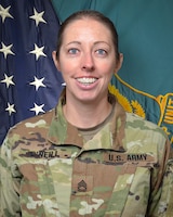 Woman in U.S. Army uniform standing in front of two flags.