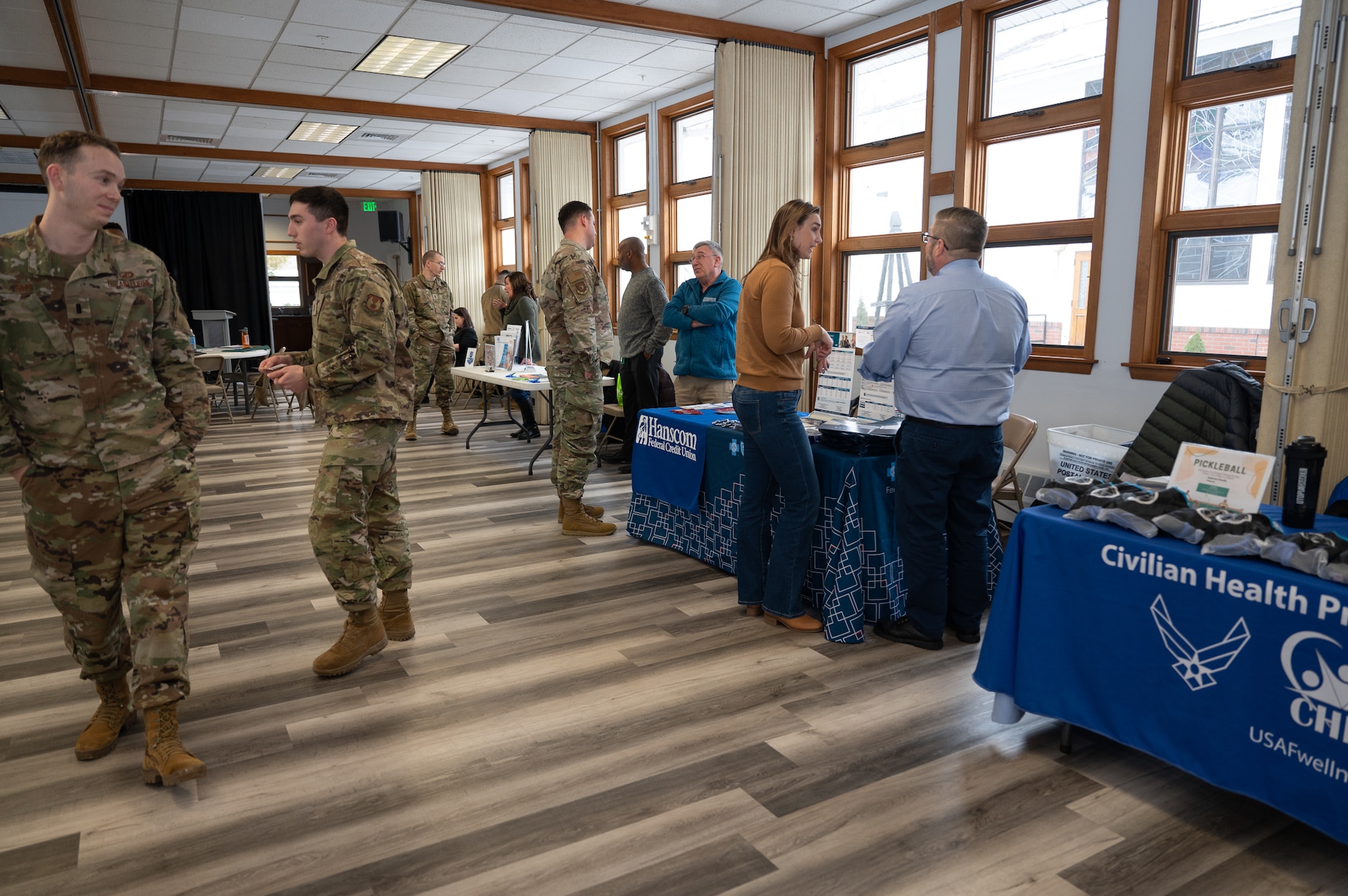 military members and civilians walk between tables and booths at the information fair.