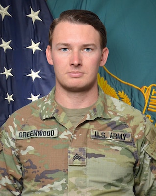 Man in U.S. Army uniform standing in front of two flags.