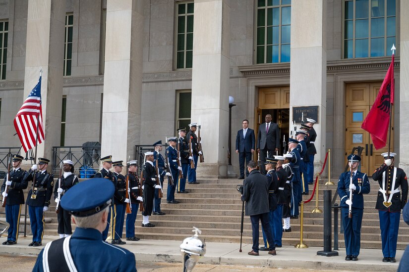 Secretary of Defense Lloyd J. Austin III stands on steps outside the Pentagon with another official, flanked by honor guard members.