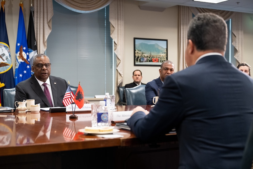 Secretary of Defense Lloyd J. Austin III speaks at a table to another official seated across from him.