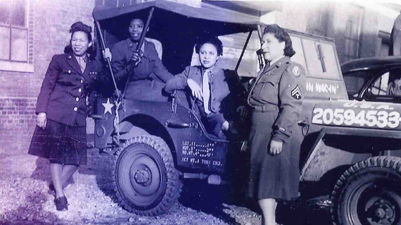 Four women dressed in military uniforms pose in a military vehicle during World War II.