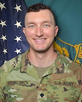 Man in U.S. Army uniform standing in front of two flags.