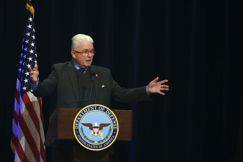 A man wearing business attire speaks while standing behind a lectern.