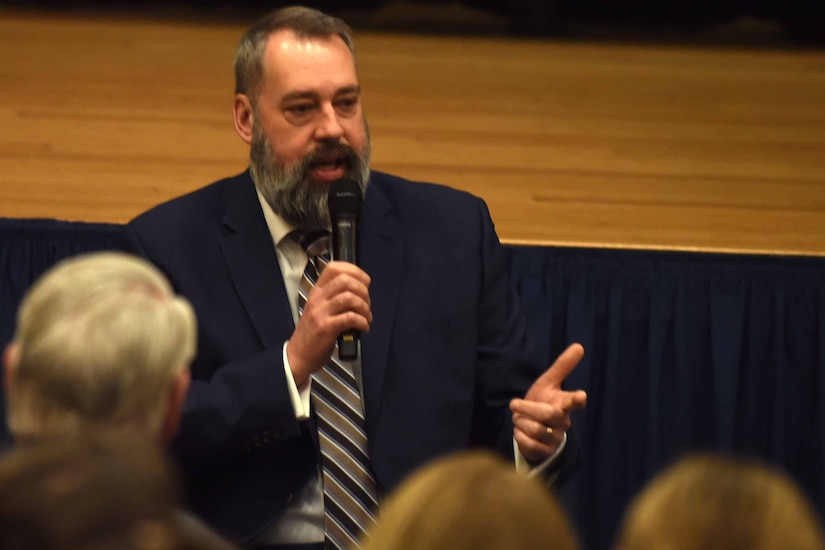 A man wearing business attire speaks in front of a crowd.