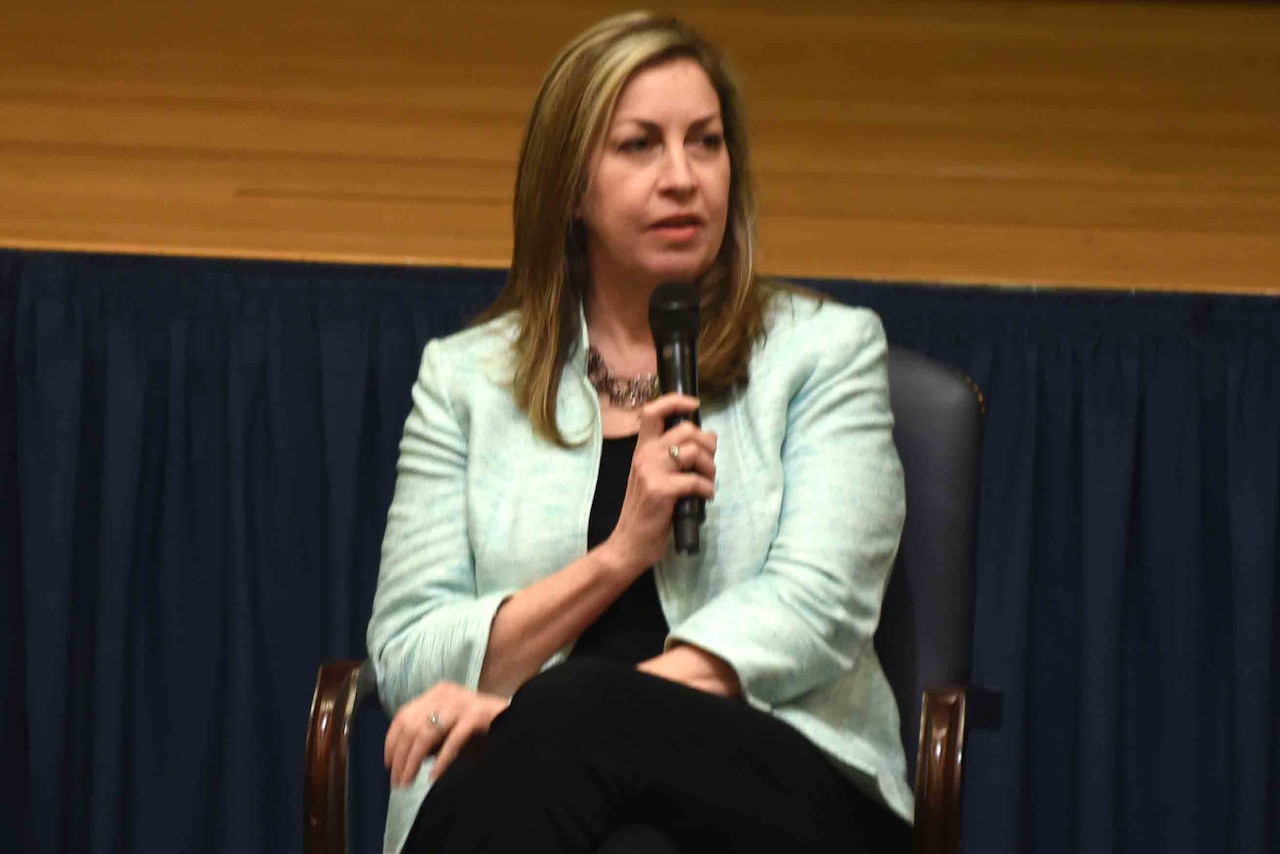 A seated woman wearing business attire speaks.