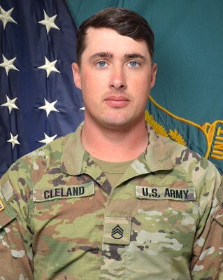 Man in U.S. Army uniform standing in front of two flags.