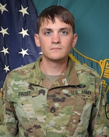 Man in U.S. Army uniform standing in front of two flags.