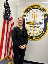 PEARL HARBOR, Hawaii (Dec. 15, 2022) Information Systems Technician 2nd Class Stephanie Hunter, Surface Combat Systems Training Command’s 2022 Junior Sailor of the Year, poses by her detachment’s logo, SCSTC Det Middle Pacific (MIDPAC). (U.S. Navy photo by Surface Combat Systems Training Command Det Middle Pacific)