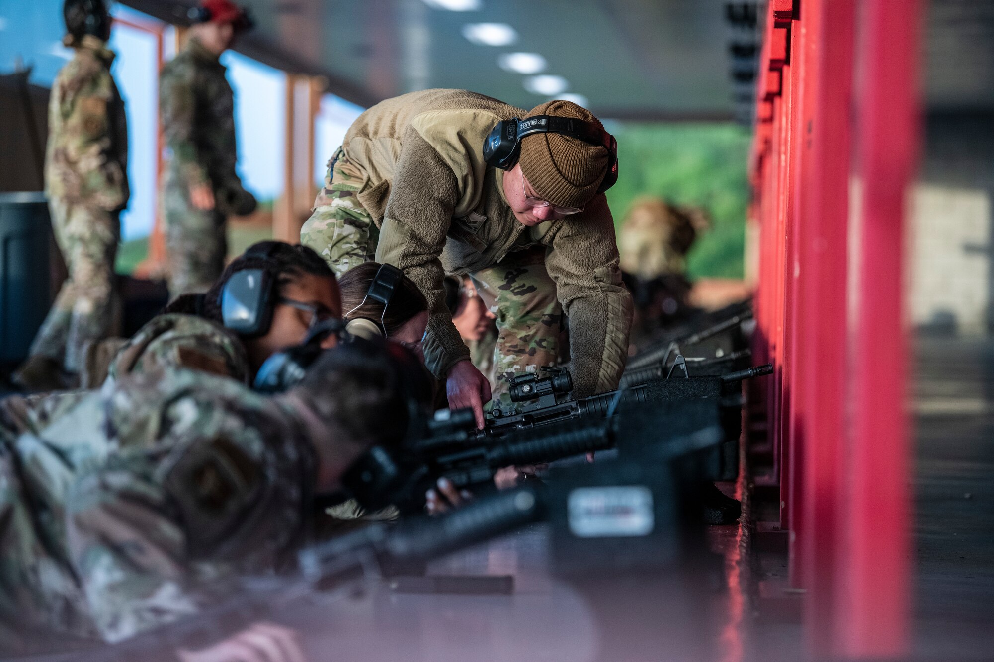 A man in uniform is bending down to assist a woman clear a weapons jam.