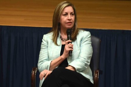 A seated woman wearing business attire speaks.