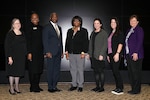 Group photo of six women and one male in front of a black screen.