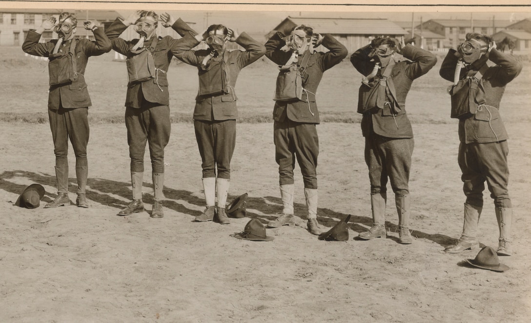 Six men work to put on gas masks.