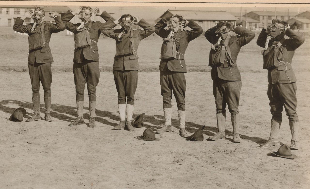 Six men work to put on gas masks.