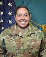 Woman in U.S. Army uniform standing in front of two flags.