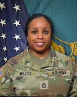 Woman in U.S. Army uniform standing in front of two flags.