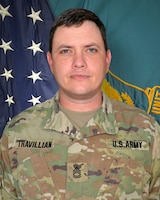 Man in U.S. Army uniform standing in front of two flags.