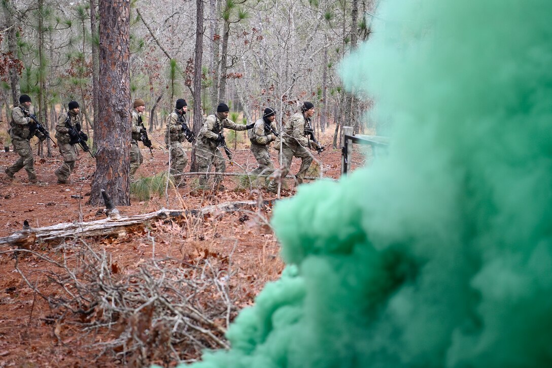 Soldiers carrying weapons advance in a line as green smoke is seen in the foreground.