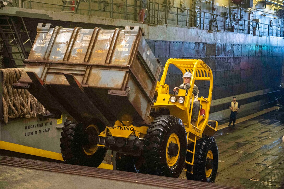 A Marine operates a forklift in the well deck of a ship.