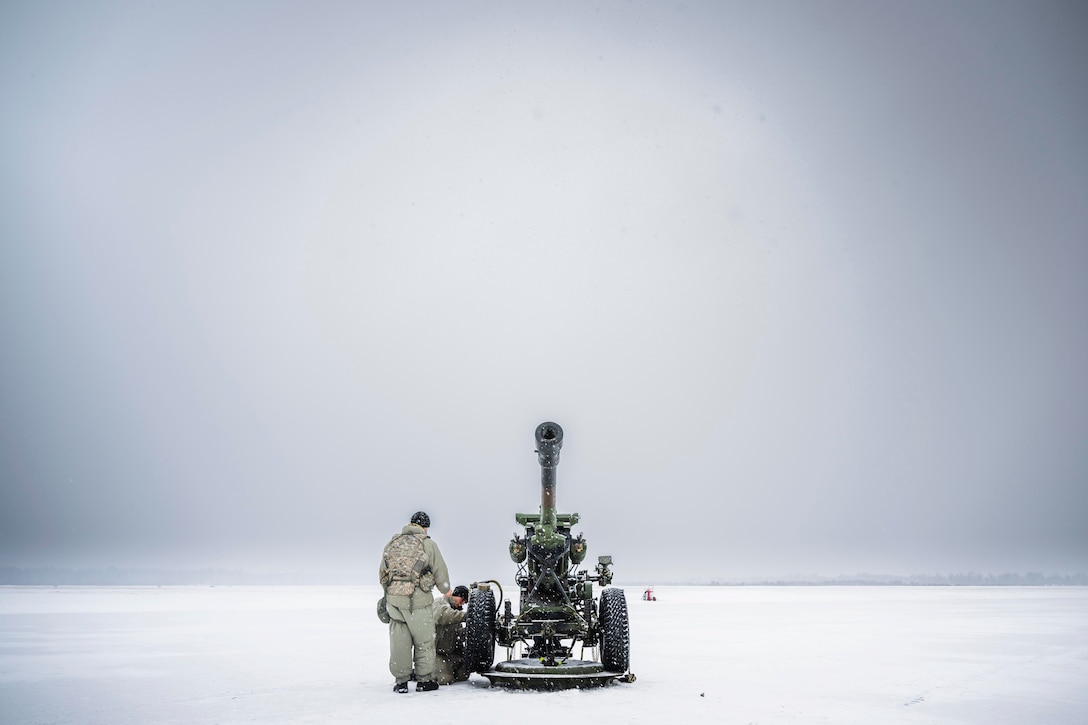 Two guardsmen work on a weapon in the snow.