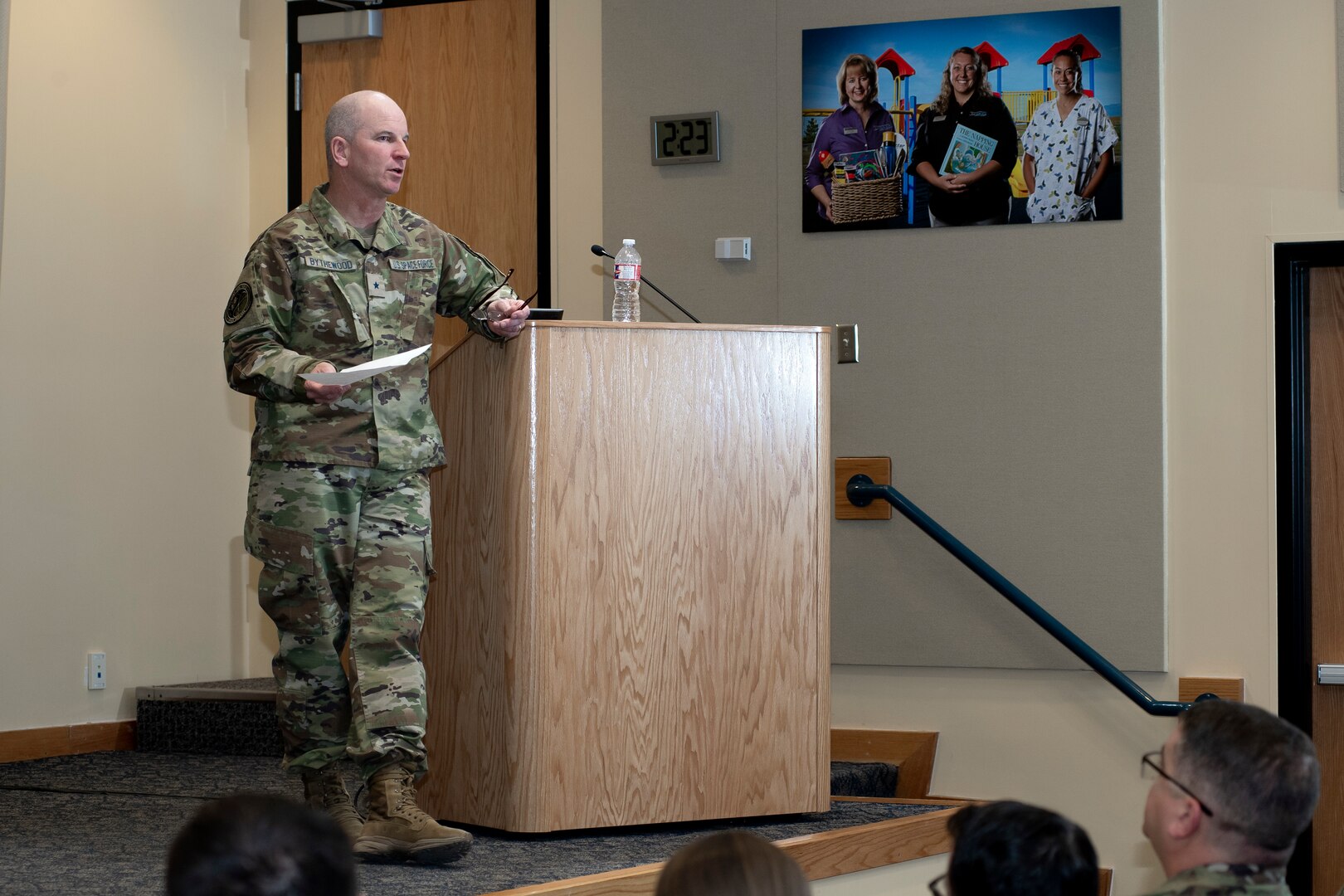 Man in uniform leaning on a podium speaks to an audience on stage