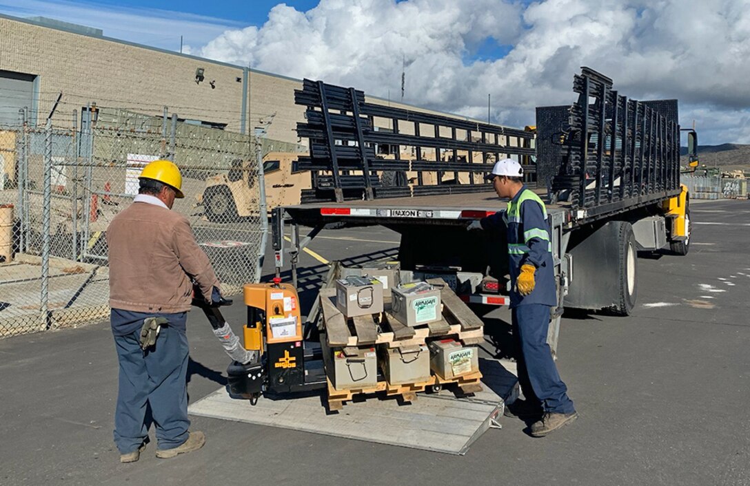Men prepare a pallet of batteries to be put onto a flatbed truck.