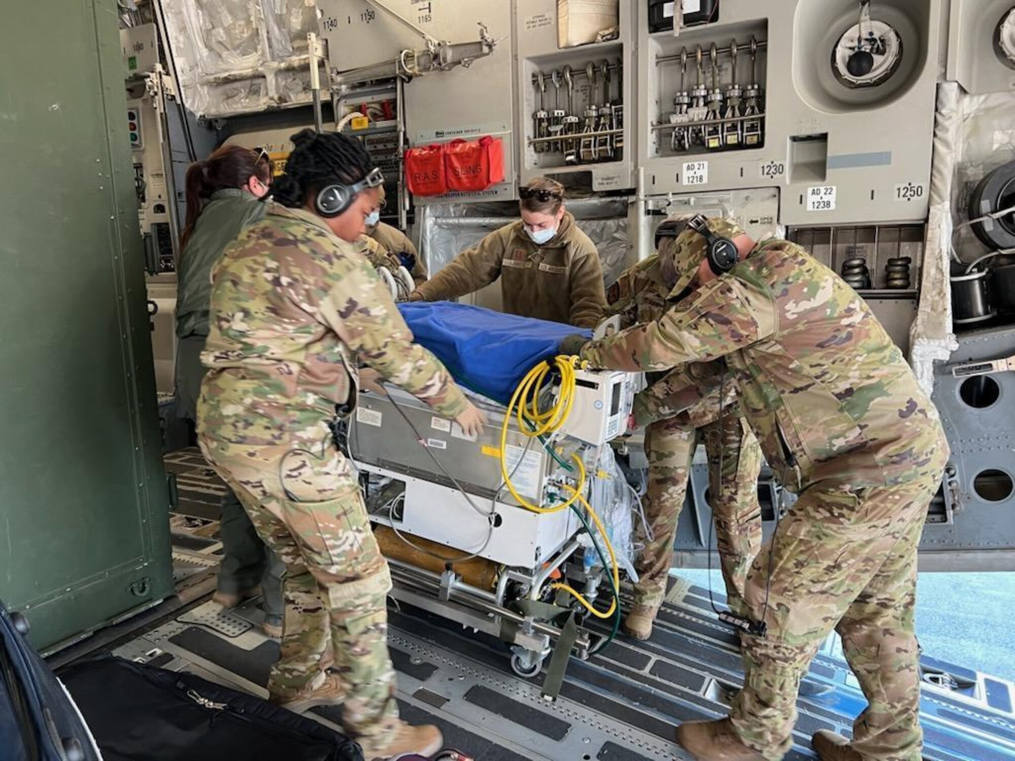 Military members pushing an incubator off of a plane to a waiting ambulance